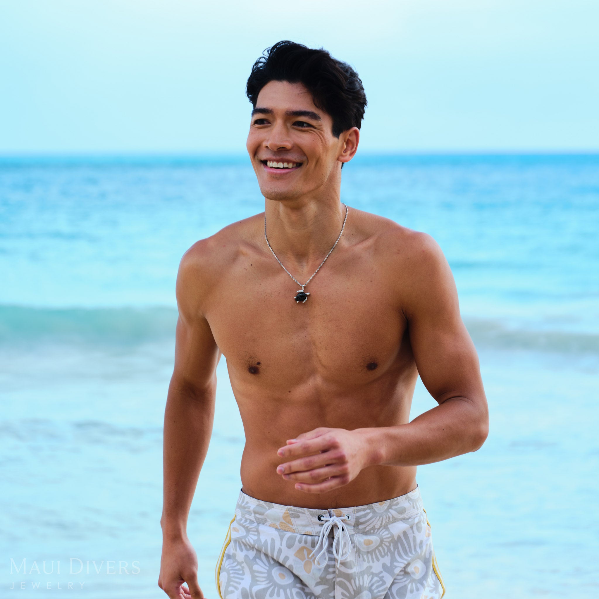 Man wearing a white gold chain with a black coral sea turtle pendant on a beach