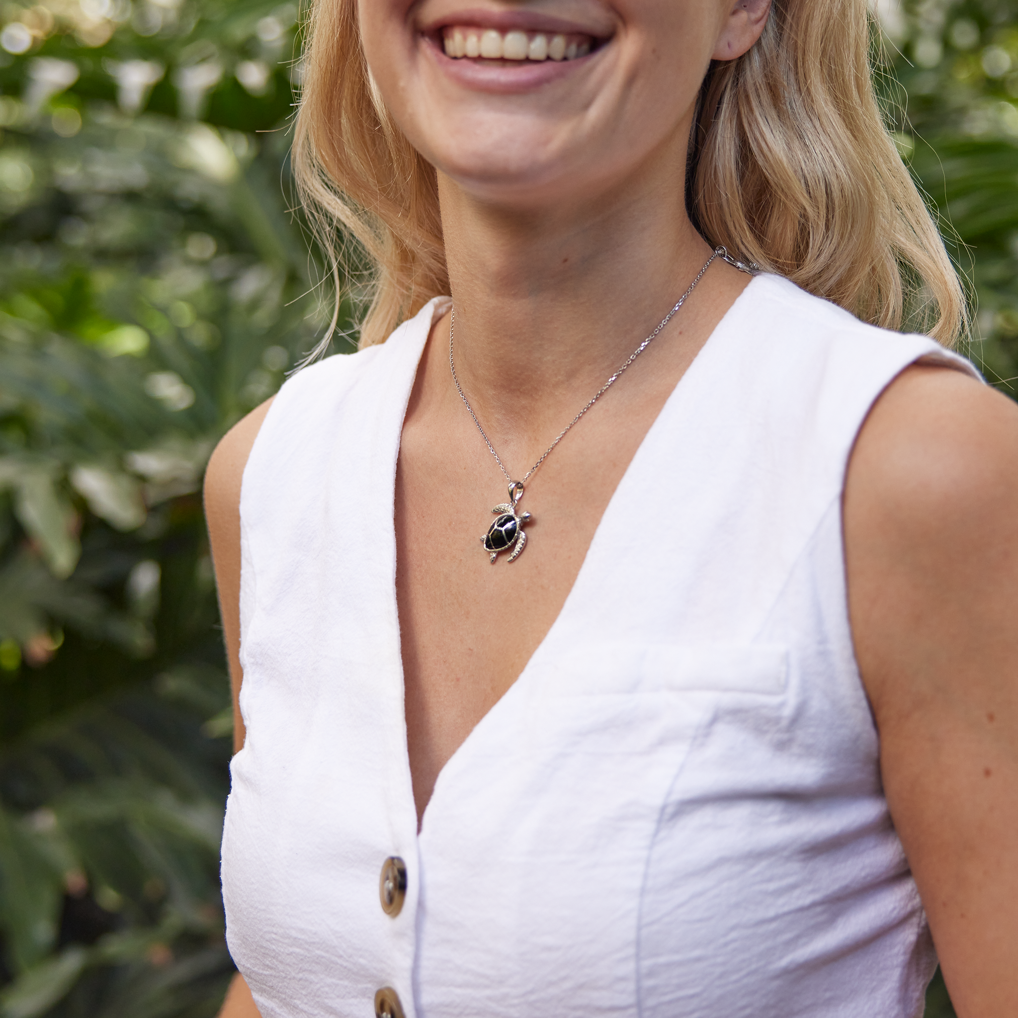 woman in white top wearing Honu Black Coral Pendant in Sterling Silver in garden