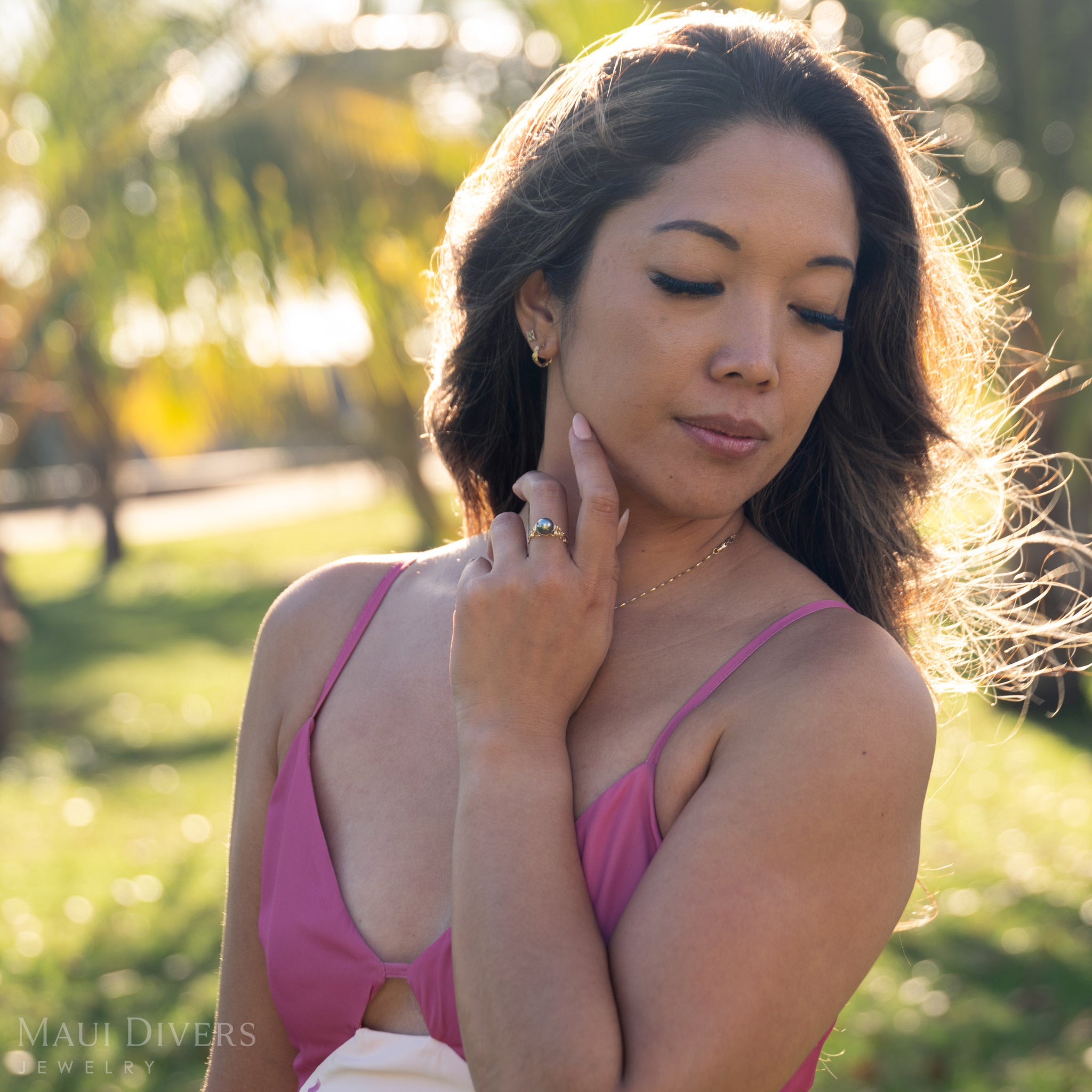 Woman in a pink dress wearing a Tahitian black pearl ring in gold outdoors with blurred greenery in the background