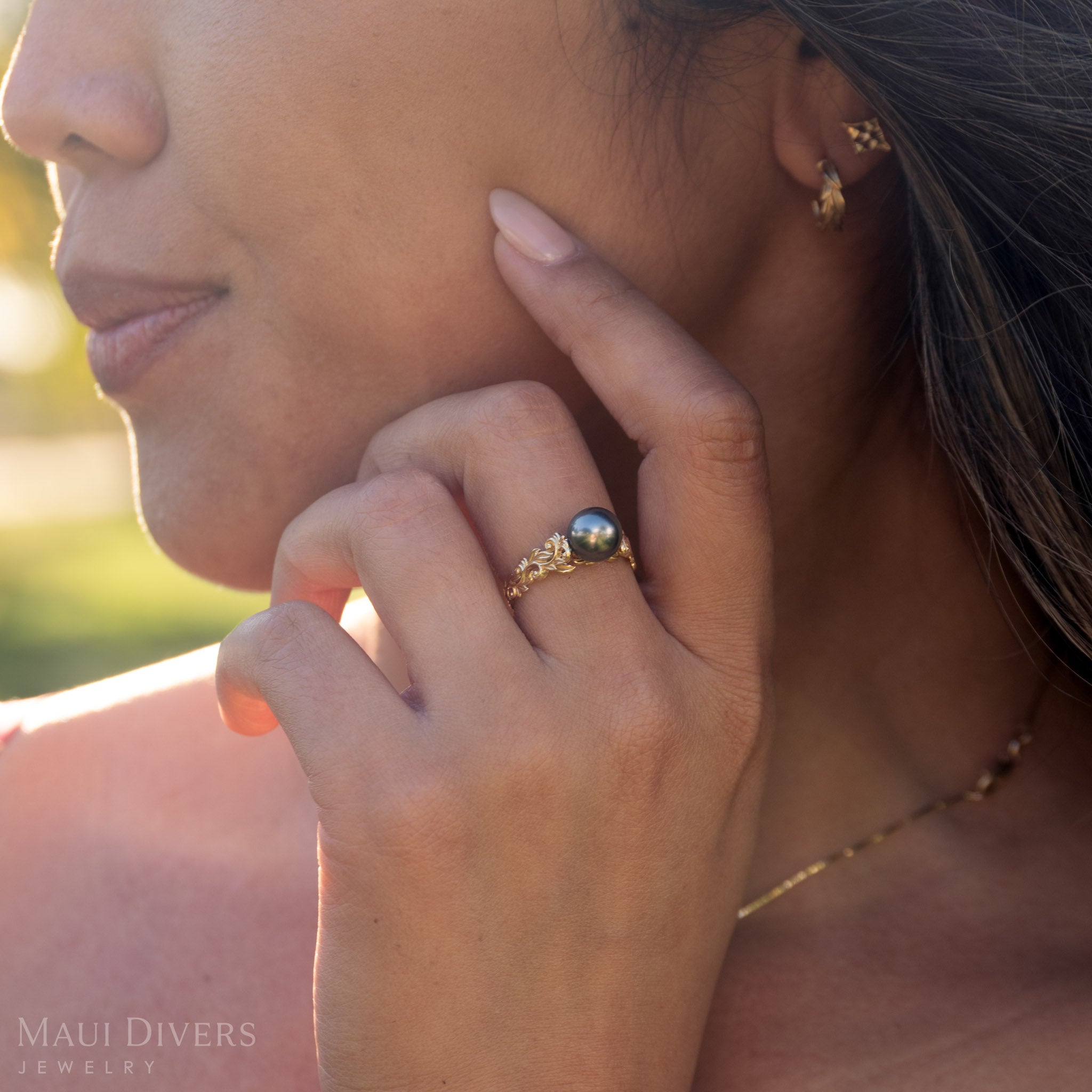 Close-up of a woman wearing a gold ring with a Tahitian black pearl, outdoors.
