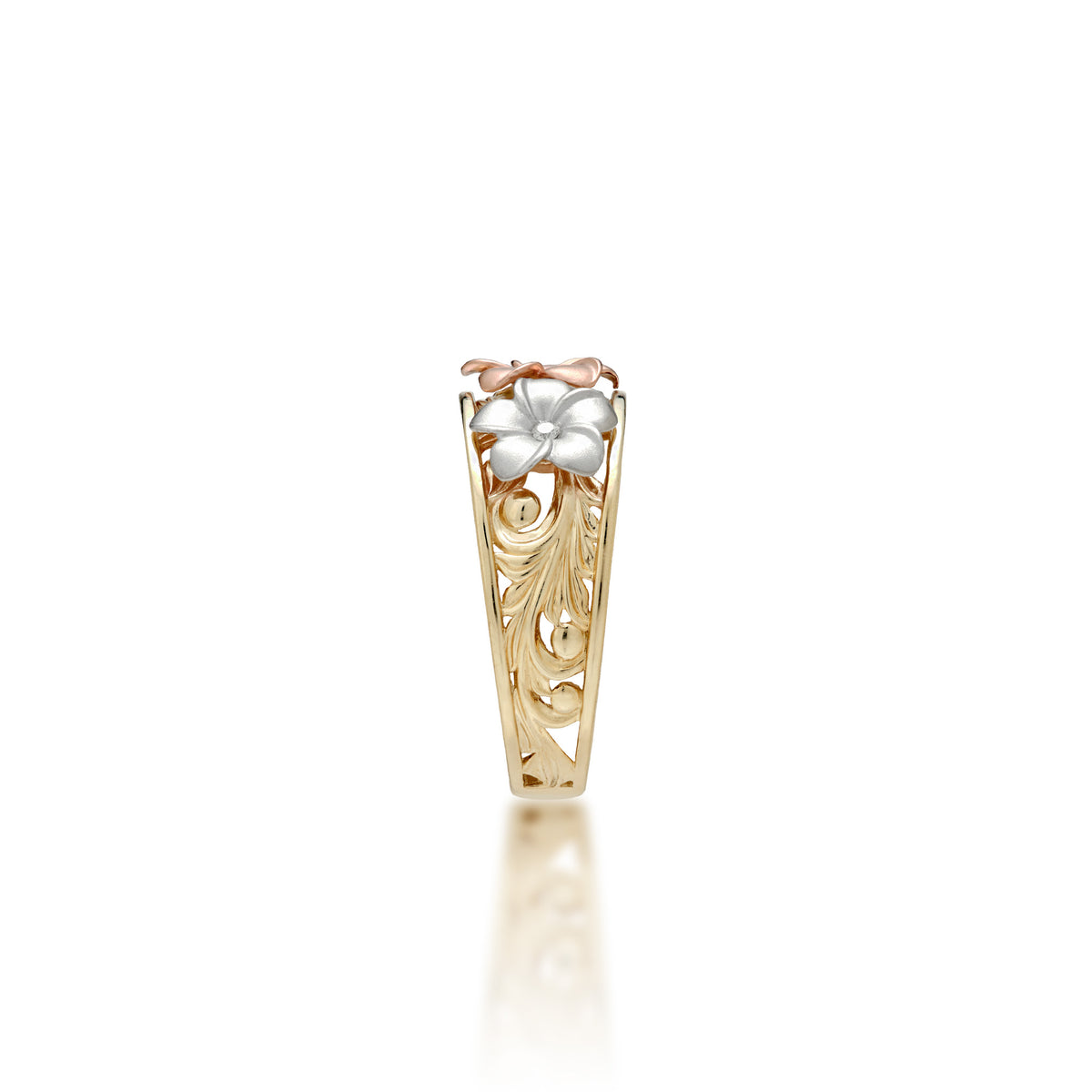 Side view of a Hawaiian Heirloom Ring with a 14k yellow gold band featuring hāpuʻu fern and maile leaf scrollwork and a single 14k diamond-accented rose gold plumeria at the top and a 14k white gold diamond-accented plumeria on the side, shown on a white background
