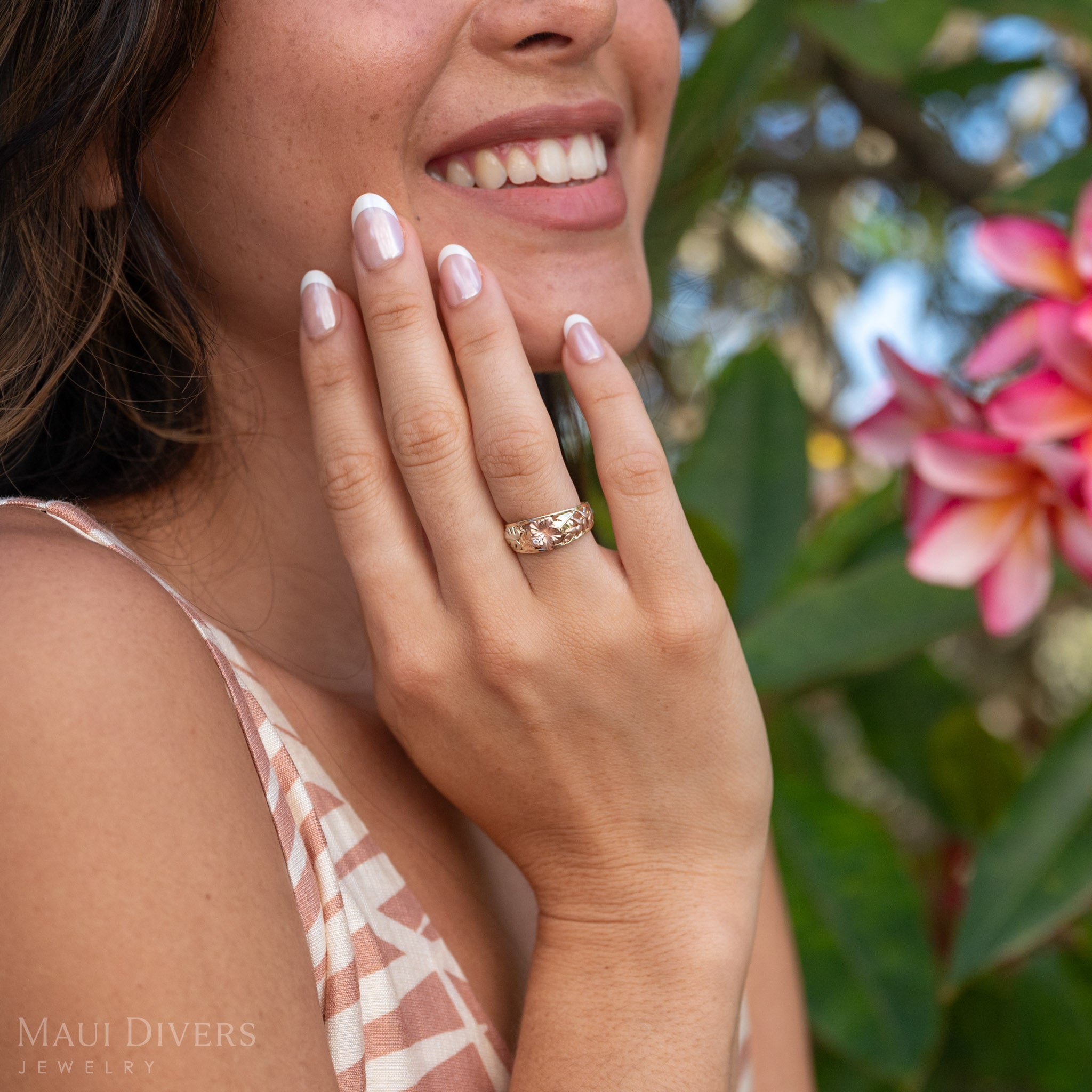 Woman with hand to her face wearing a Hawaiian Gardens Hibiscus Ring in 14k Yellow, Rose, and Green Gold displaying monstera, heliconia, and hibiscus flowers. 