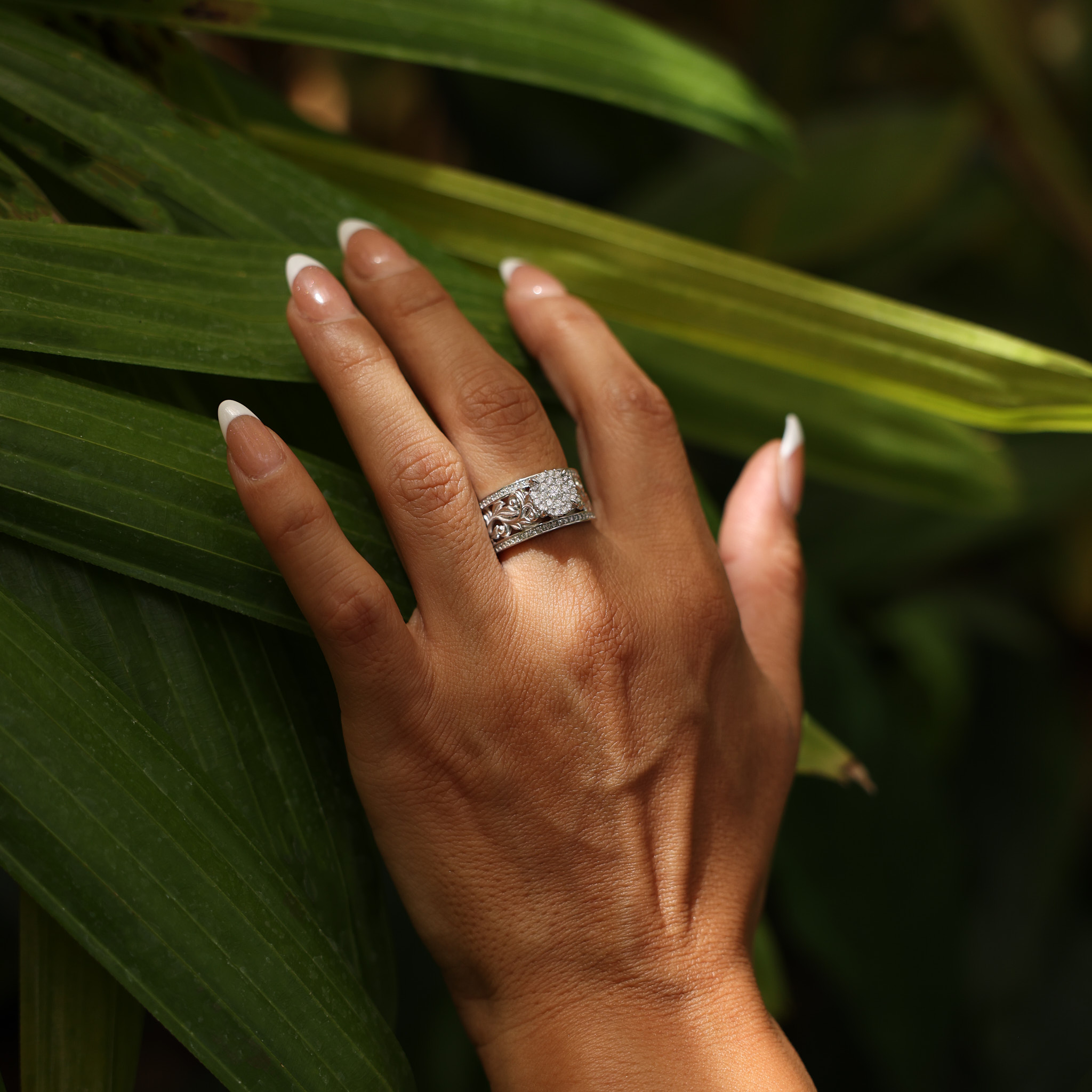 Close up of Hawaiian Heirloom Engagement Ring in White Gold with Diamonds on woman's hand with tropical forest background