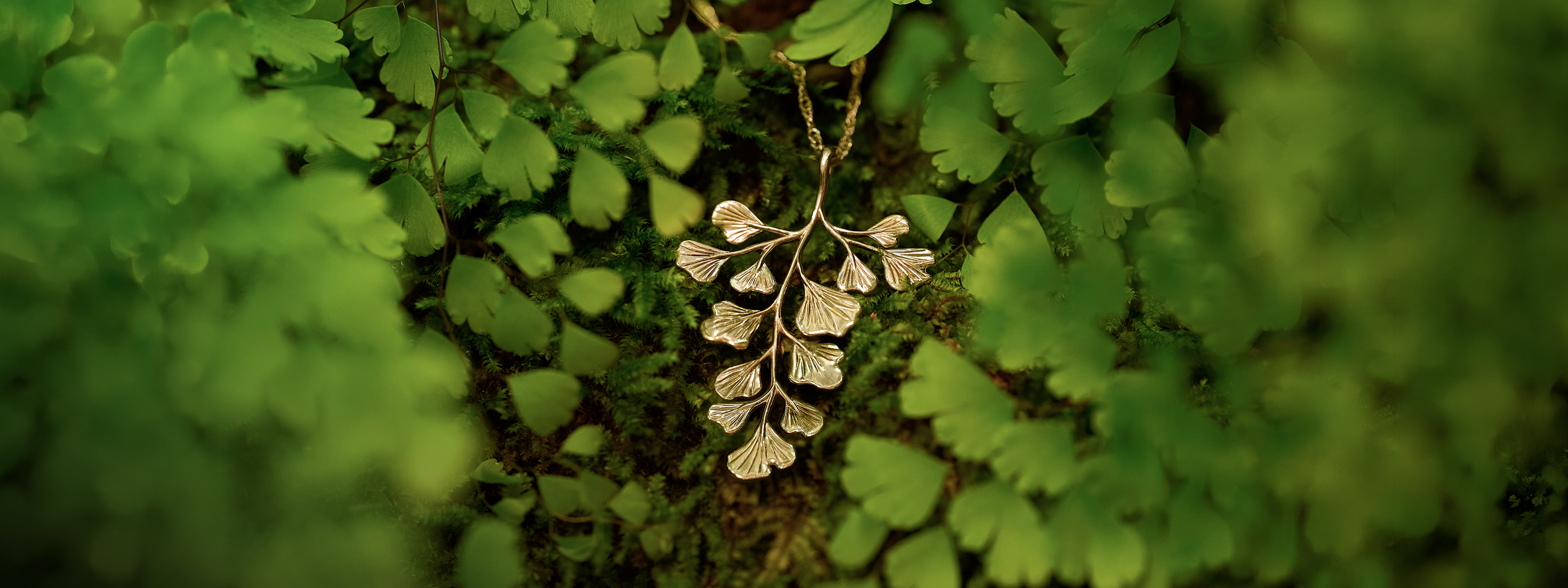 Maiden Hair Pendant in 14k yellow gold on a singapore chain laying on moss with maiden hair ferns around it