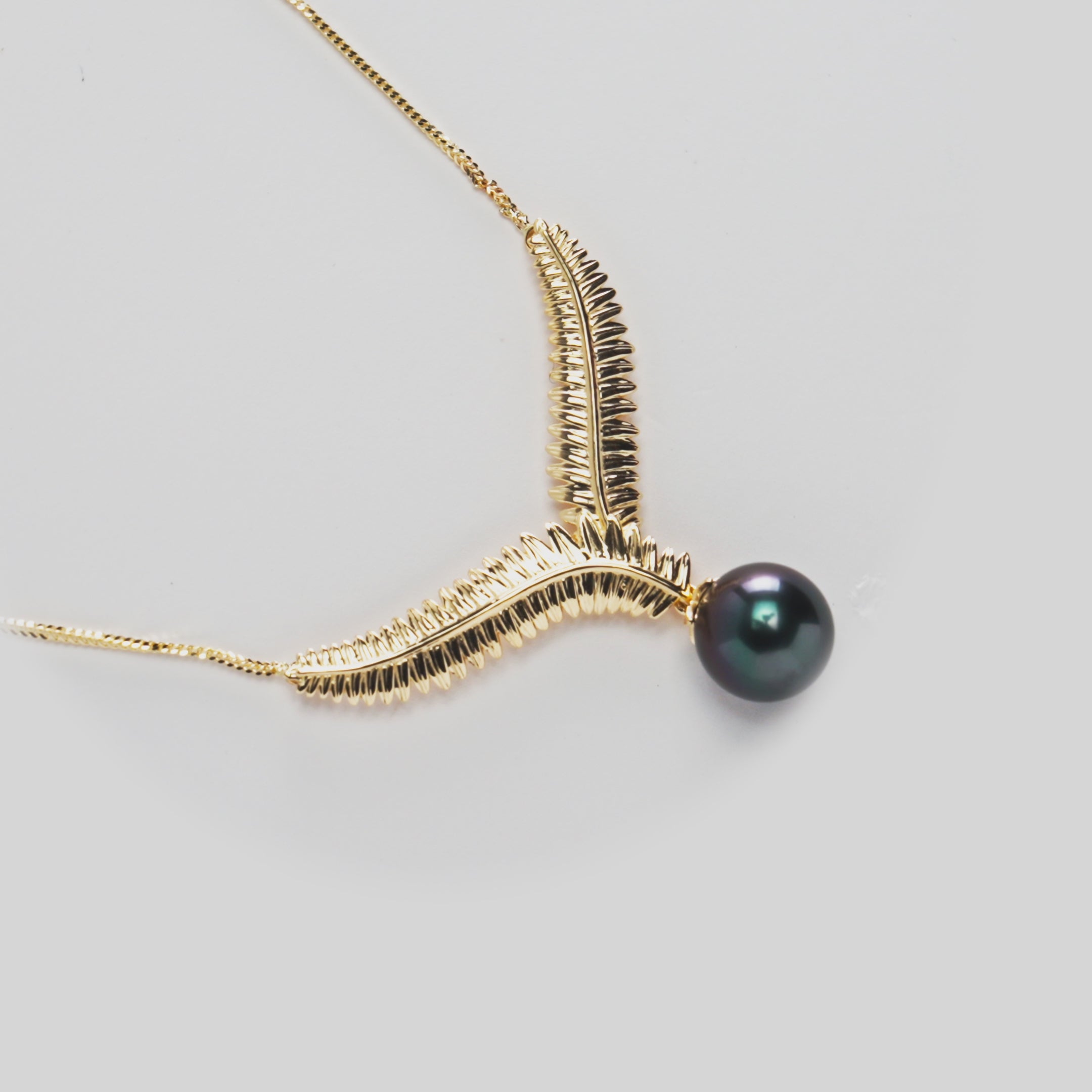Close-up of a Kupukupu Fern Tahitian Black Pearl Necklace in 14k Yellow Gold rotating on a white background